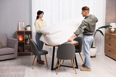 Photo of Couple putting white tablecloth on table at home