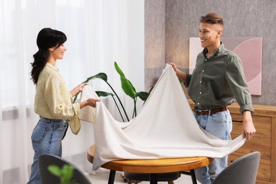 Photo of Couple putting white tablecloth on table at home