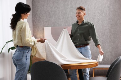 Photo of Couple putting white tablecloth on table at home