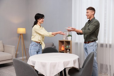 Photo of Couple putting plates on table with tablecloth at home