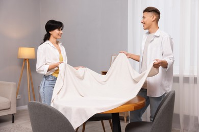 Photo of Couple putting white tablecloth on table at home