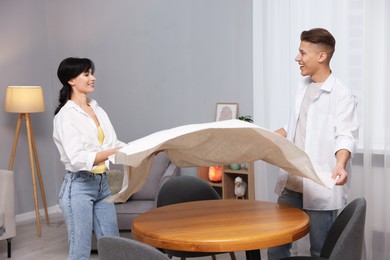 Photo of Couple putting white tablecloth on table at home