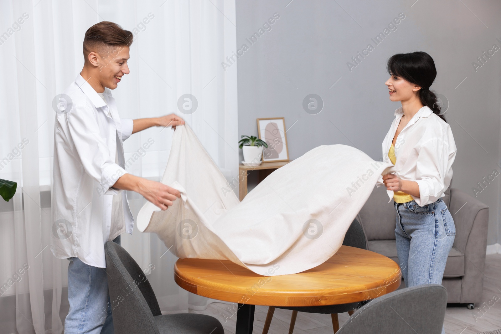 Photo of Couple putting white tablecloth on table at home