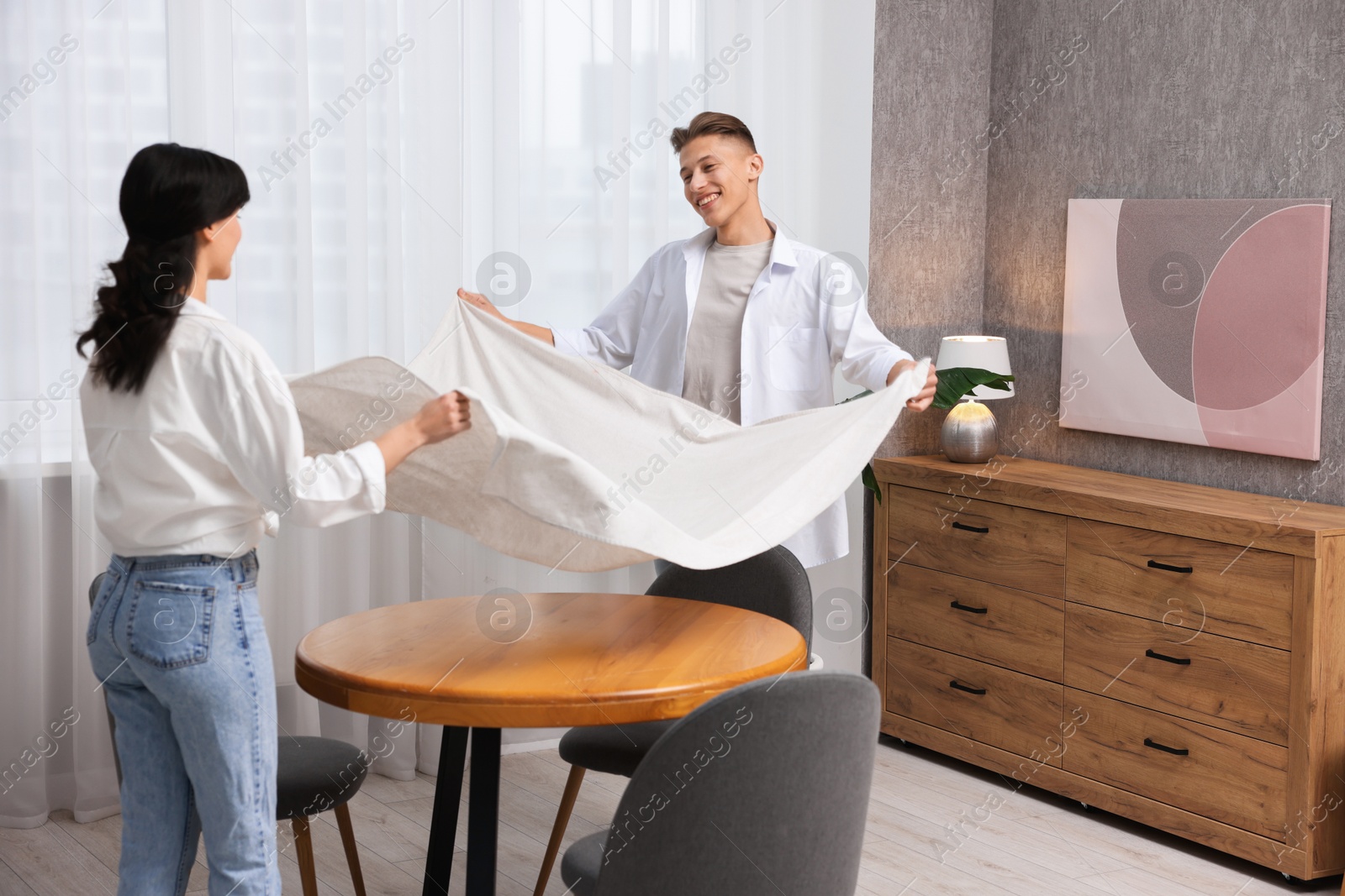 Photo of Couple putting white tablecloth on table at home