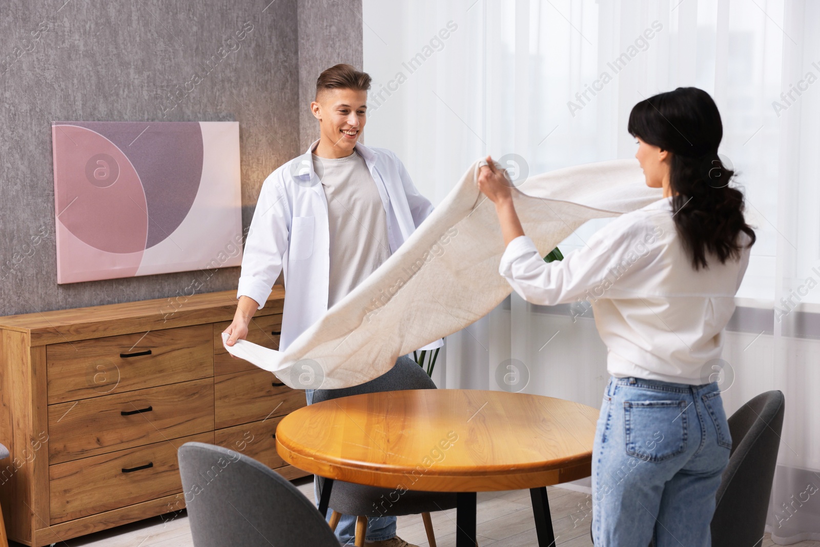 Photo of Couple putting white tablecloth on table at home