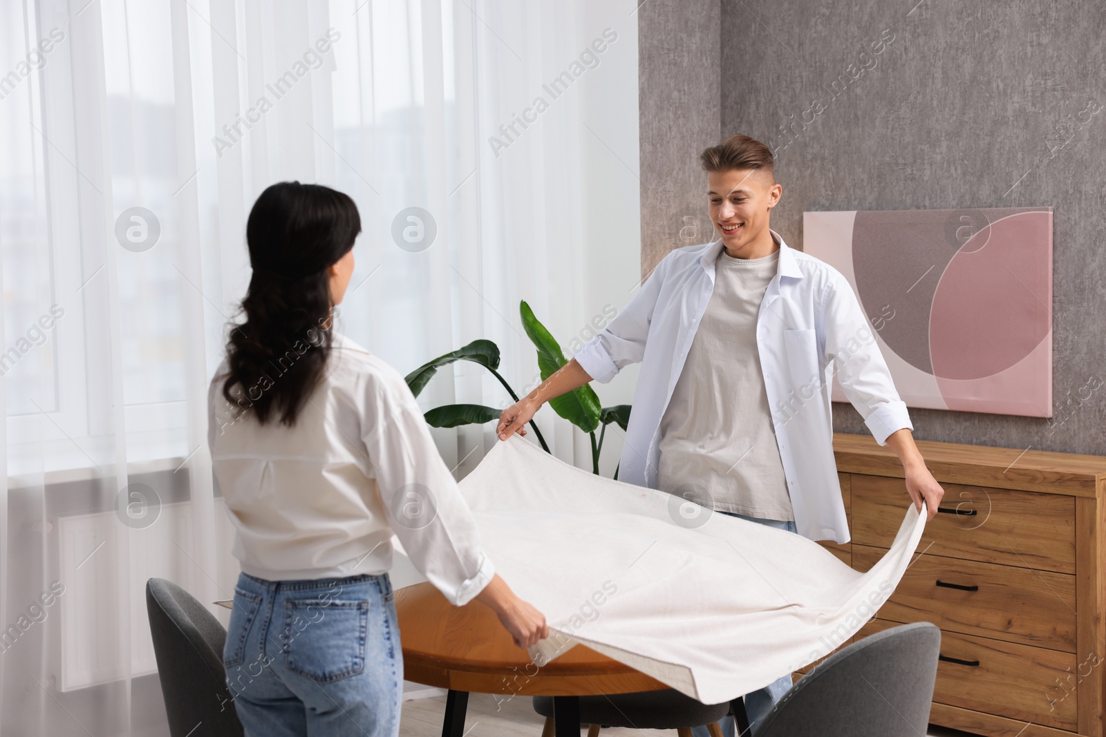 Photo of Couple putting white tablecloth on table at home