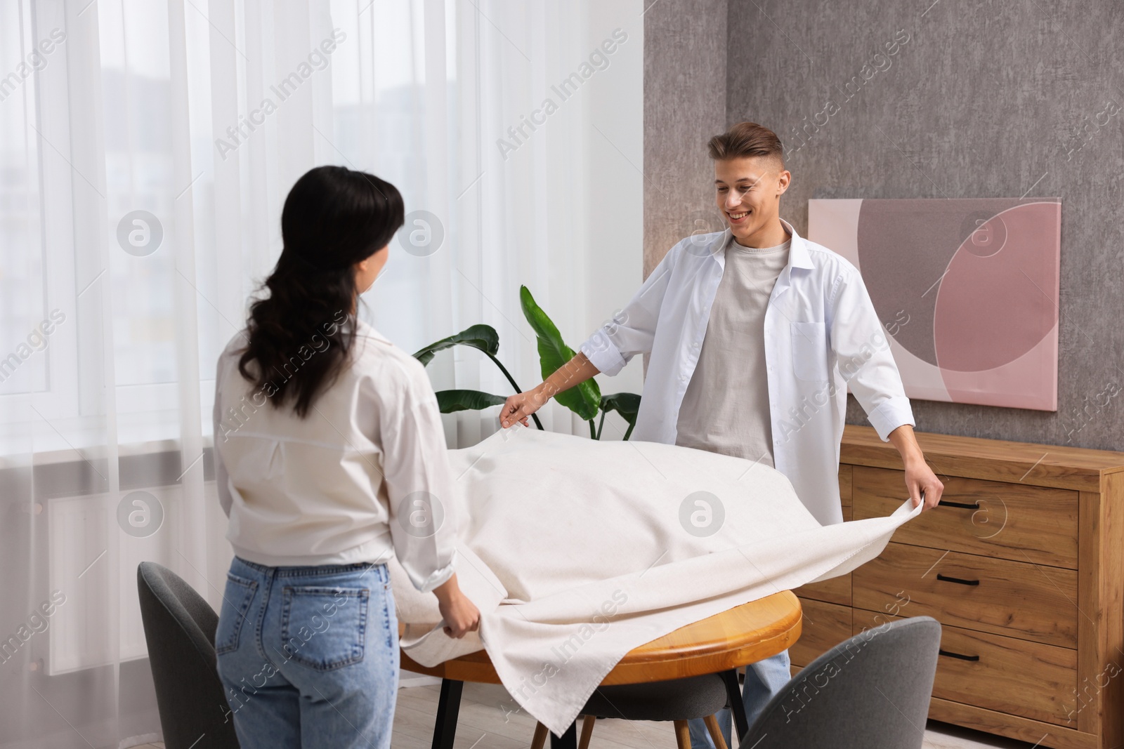 Photo of Couple putting white tablecloth on table at home