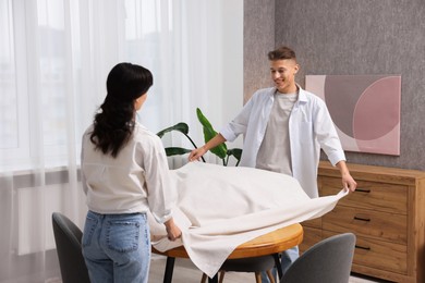 Photo of Couple putting white tablecloth on table at home