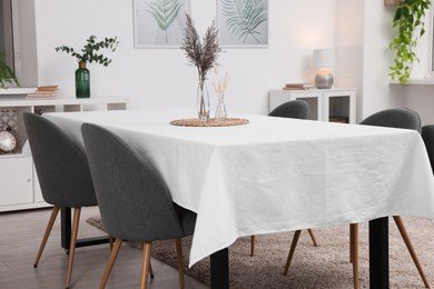 Photo of Table with white tablecloth, dried flowers in vases and chairs in stylish room. Interior design