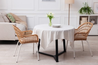 Photo of Table with white tablecloth, flowers in vase and chairs in stylish room. Interior design