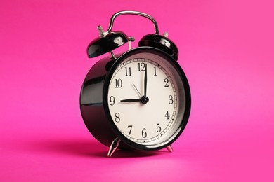 Photo of One black alarm clock on bright pink background