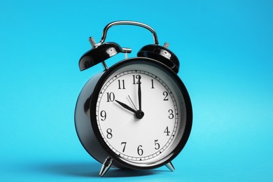 Photo of One black alarm clock on light blue background