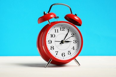 Photo of One red alarm clock on white wooden table against light blue background