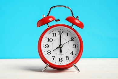 Photo of One red alarm clock on white wooden table against light blue background