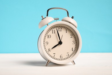 Photo of One alarm clock on white wooden table against light blue background