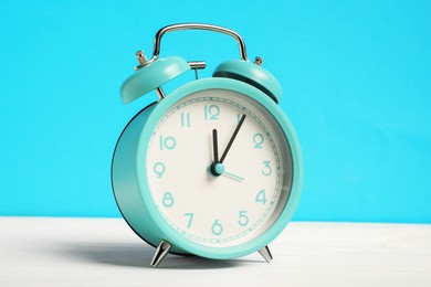 Photo of One turquoise alarm clock on white wooden table against light blue background