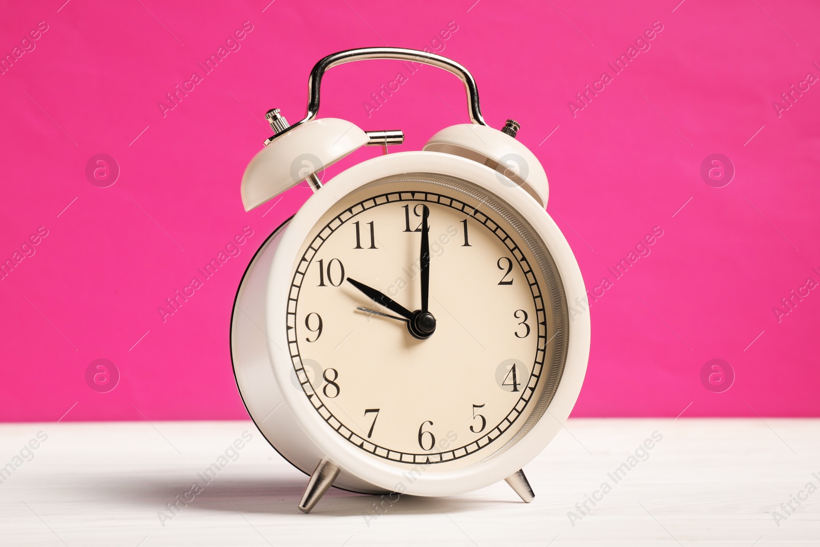 One alarm clock on white wooden table against bright pink background Photo of One alarm clock on white wooden table against bright pink background