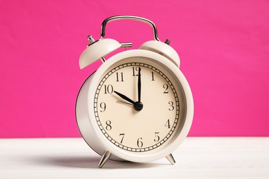 Photo of One alarm clock on white wooden table against bright pink background