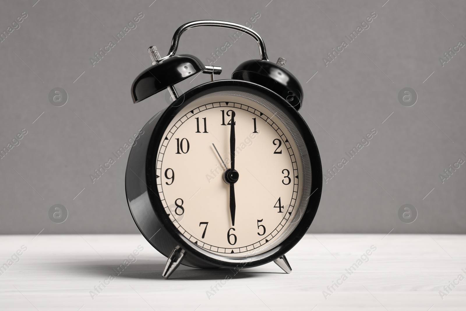 Photo of One black alarm clock on white wooden table against grey background