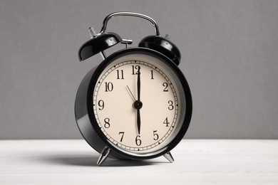 Photo of One black alarm clock on white wooden table against grey background