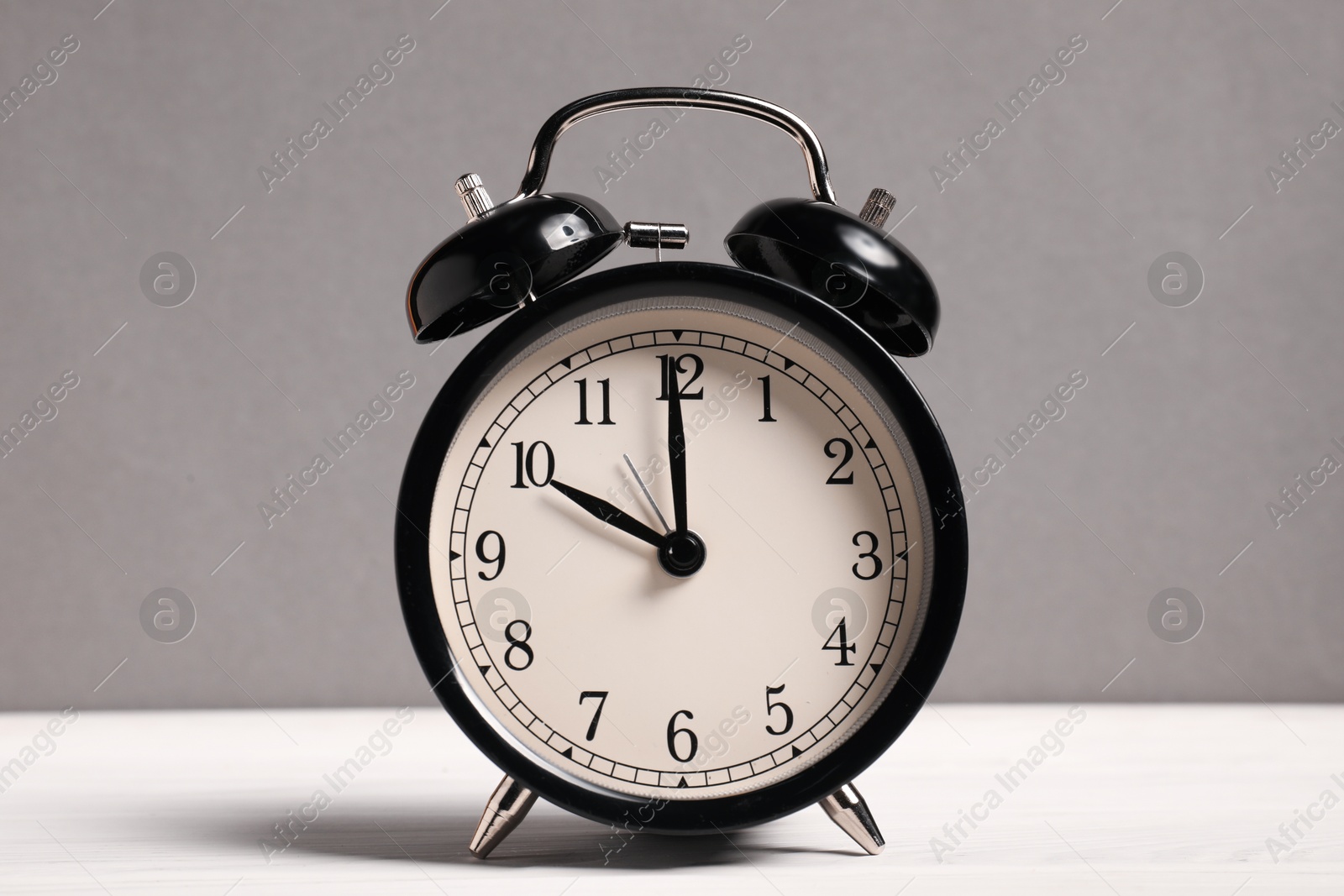 One black alarm clock on white wooden table against grey background Photo of One black alarm clock on white wooden table against grey background