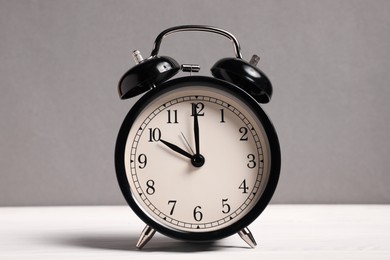 Photo of One black alarm clock on white wooden table against grey background