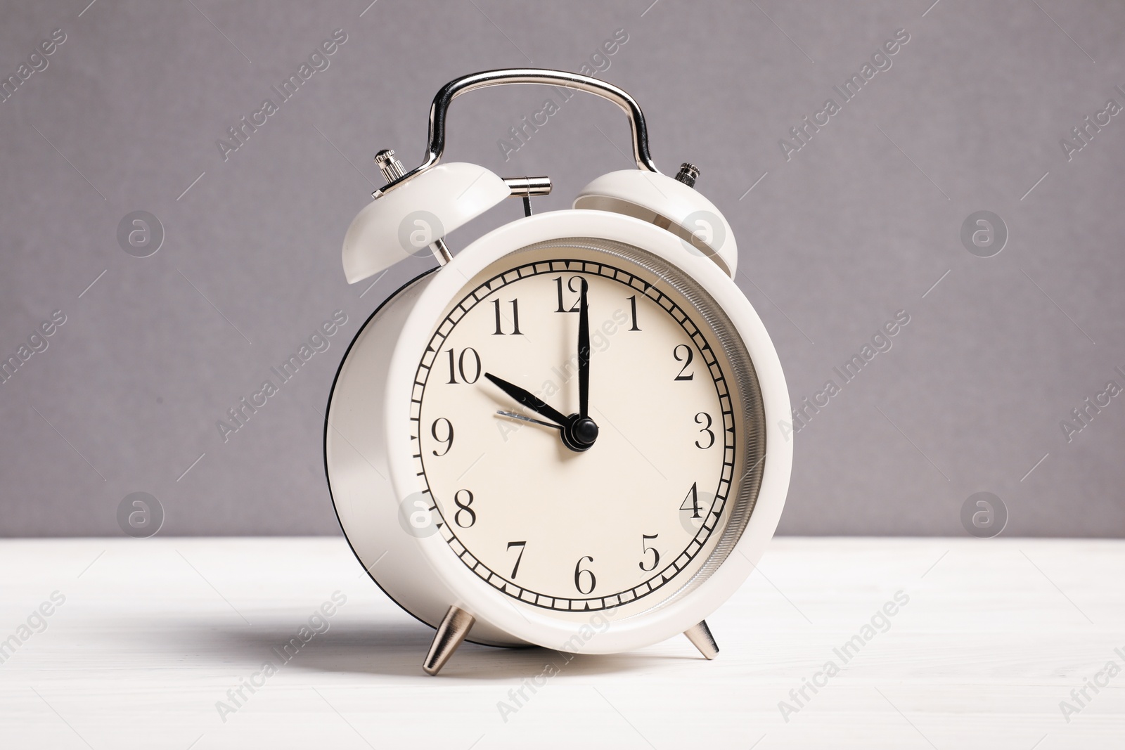 One alarm clock on white wooden table against grey background Photo of One alarm clock on white wooden table against grey background
