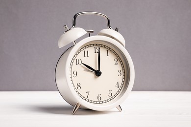 Photo of One alarm clock on white wooden table against grey background
