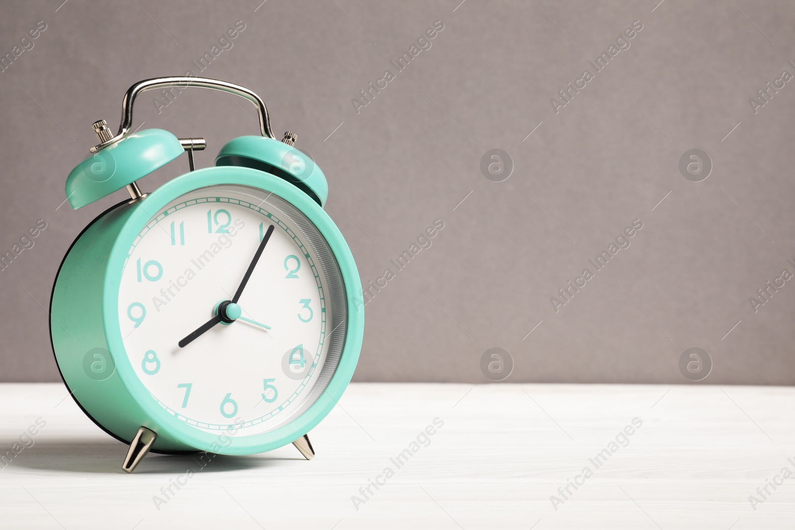 One turquoise alarm clock on white wooden table against grey background, space for text Photo of One turquoise alarm clock on white wooden table against grey background, space for text