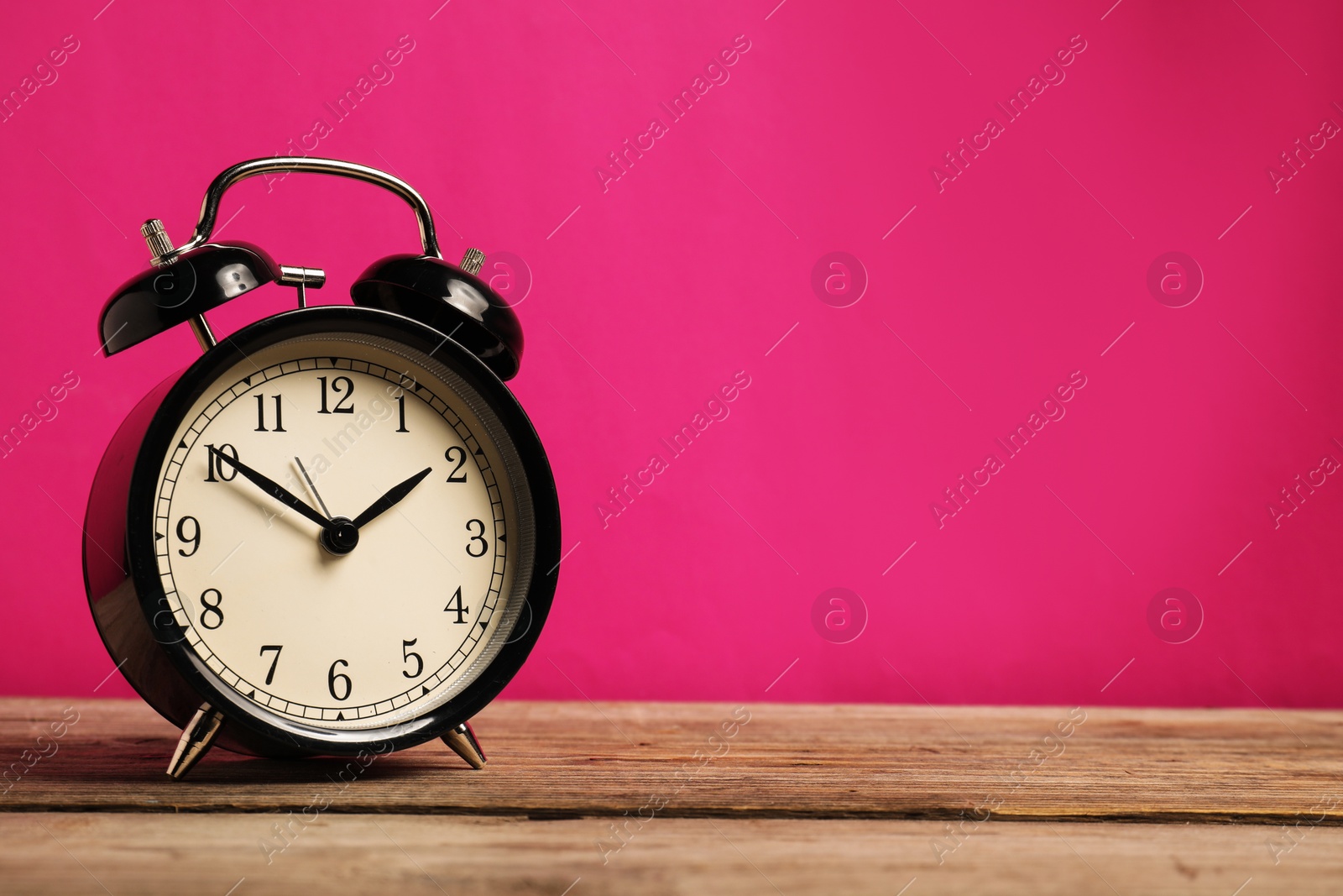 One black alarm clock on wooden table against bright pink background, space for text Photo of One black alarm clock on wooden table against bright pink background, space for text