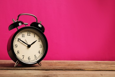 Photo of One black alarm clock on wooden table against bright pink background, space for text