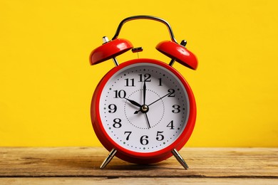 Photo of One red alarm clock on wooden table against yellow background