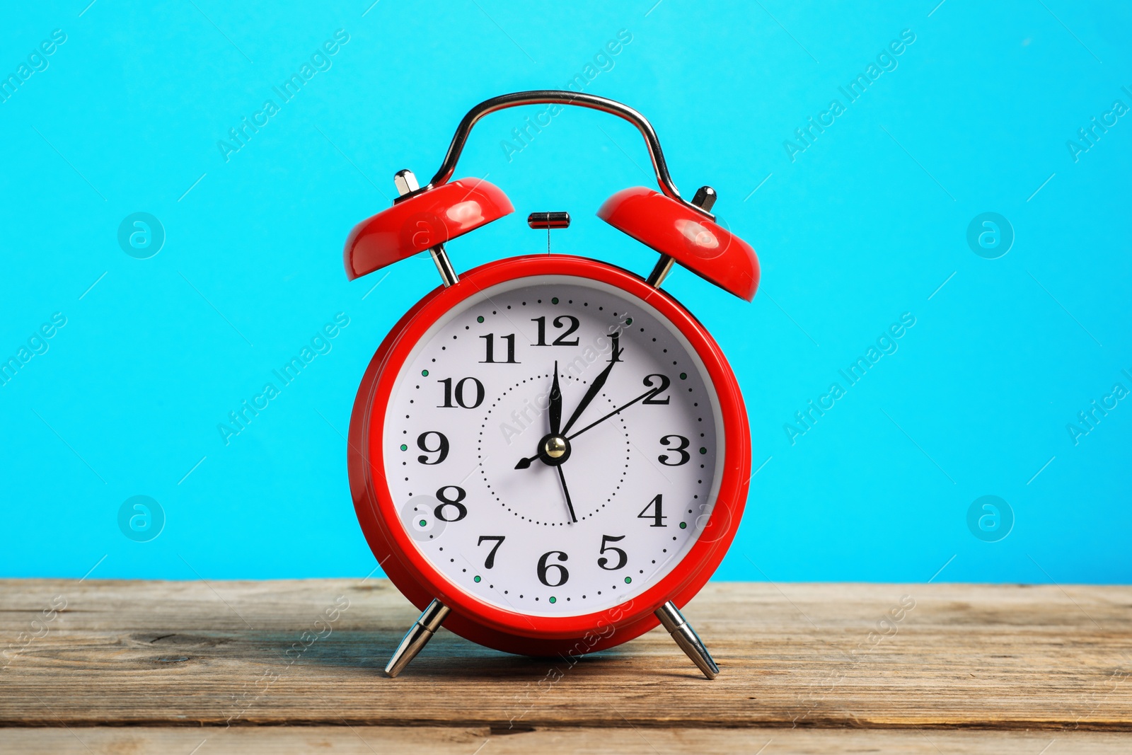 One red alarm clock on wooden table against light blue background Photo of One red alarm clock on wooden table against light blue background