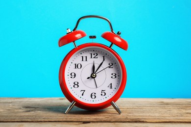 Photo of One red alarm clock on wooden table against light blue background