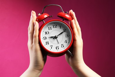 Photo of Woman with red alarm clock on bright pink background, closeup