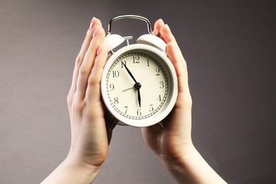 Photo of Woman with white alarm clock on grey background, closeup