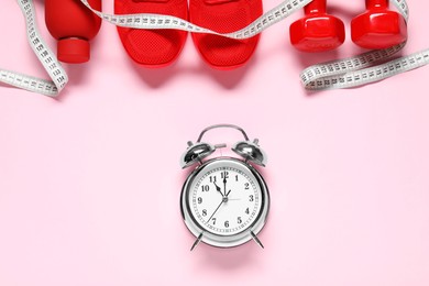 Photo of Alarm clock, sneakers, dumbbells, measuring tape and water bottle on pink background, flat lay