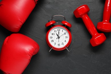 Photo of Alarm clock, boxing gloves and dumbbells on black background, flat lay