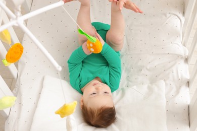 Photo of Cute little baby playing with cot mobile in crib at home, closeup