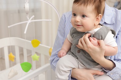 Photo of Mother holding her little baby, closeup. Crib with cot mobile in nursery