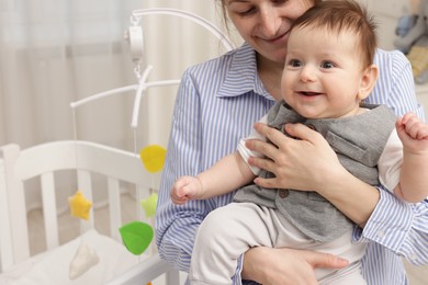 Photo of Mother holding her little baby, closeup. Crib with cot mobile in nursery