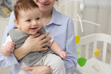 Photo of Mother holding her little baby, closeup. Crib with cot mobile in nursery