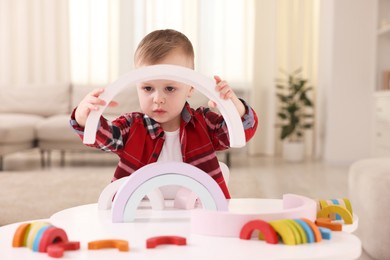 Photo of Motor skills development. Little boy playing with toys at white table indoors