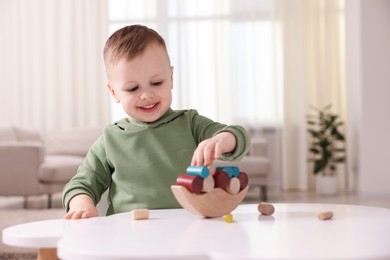 Photo of Motor skills development. Little boy playing with balance toy at white table indoors