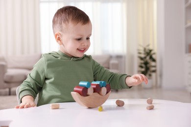 Photo of Motor skills development. Little boy playing with balance toy at white table indoors