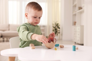 Photo of Motor skills development. Little boy playing with balance toy at white table indoors