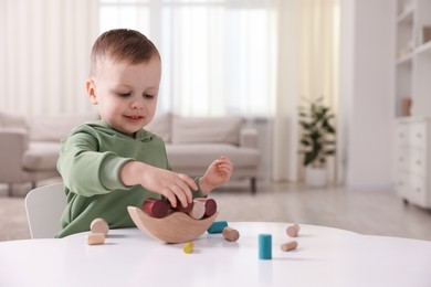 Photo of Motor skills development. Little boy playing with balance toy at white table indoors