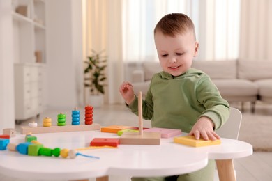 Photo of Motor skills development. Little boy playing with stacking toy at white table indoors