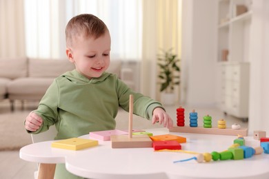 Photo of Motor skills development. Little boy playing with stacking toy at white table indoors