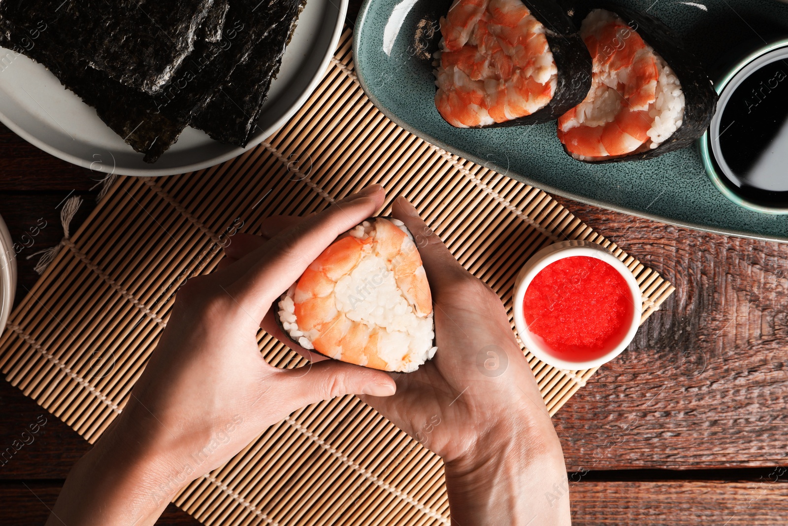 Woman holding tasty onigiri (Japanese rice ball) with shrimp at wooden table, top view Photo of Woman holding tasty onigiri (Japanese rice ball) with shrimp at wooden table, top view